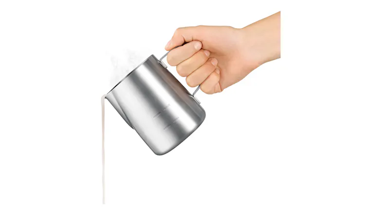 A hand pouring milk from a steel pitcher A hand pouring milk from a steel pitcher
