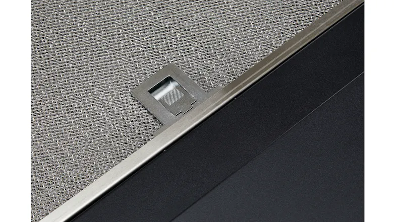 Close-up of rangehood mesh filter with metal pull tab and black panel edge Close-up of rangehood mesh filter with metal pull tab and black panel edge