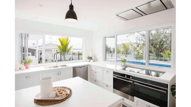 White kitchen with corner windows, a built-in oven, an induction cooktop, and a stainless steel dishwasher beneath the sink White kitchen with corner windows, a built-in oven, an induction cooktop, and a stainless steel dishwasher beneath the sink