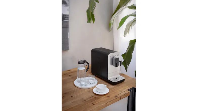 Wooden table setting featuring the coffee machine alongside a water carafe and cups Wooden table setting featuring the coffee machine alongside a water carafe and cups