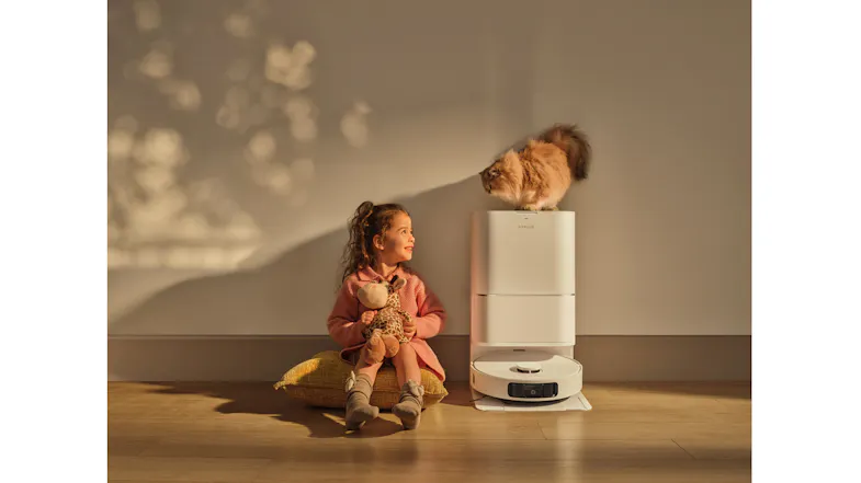 A child sitting near a white docking station with a fluffy cat A child sitting near a white docking station with a fluffy cat