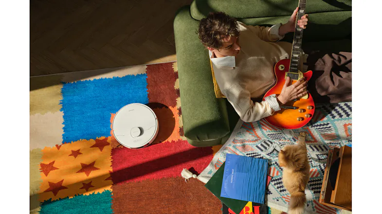 Low-angle view featuring a robot vacuum cleaning near a rug Low-angle view featuring a robot vacuum cleaning near a rug