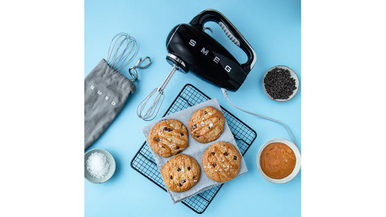 A blue kitchen counter showing freshly baked cookies next to a hand mixer A blue kitchen counter showing freshly baked cookies next to a hand mixer