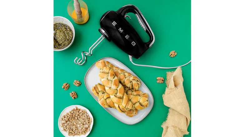 Smeg hand mixer with braided pesto bread and walnuts on a green surface Smeg hand mixer with braided pesto bread and walnuts on a green surface