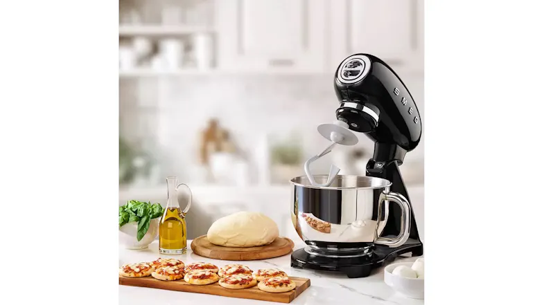 Lifestyle scene of the glossy black Smeg stand mixer on a kitchen counter with the dough hook attached Lifestyle scene of the glossy black Smeg stand mixer on a kitchen counter with the dough hook attached