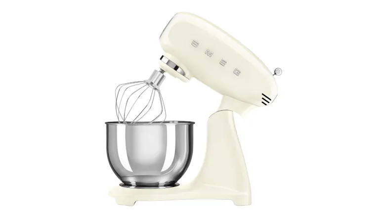 Side angle of the Smeg cream stand mixer with tilt head raised and wire whisk attached above a stainless steel bowl Side angle of the Smeg cream stand mixer with tilt head raised and wire whisk attached above a stainless steel bowl