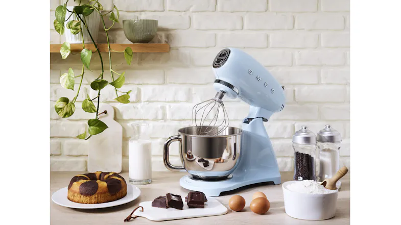 Stand mixer with whisk attachment and stainless steel bowl on a countertop against a white brick wall Stand mixer with whisk attachment and stainless steel bowl on a countertop against a white brick wall