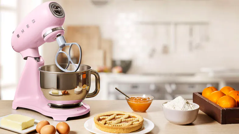 Glossy pink Smeg stand mixer with tilt head raised and flat beater attachment over a stainless steel bowl Glossy pink Smeg stand mixer with tilt head raised and flat beater attachment over a stainless steel bowl