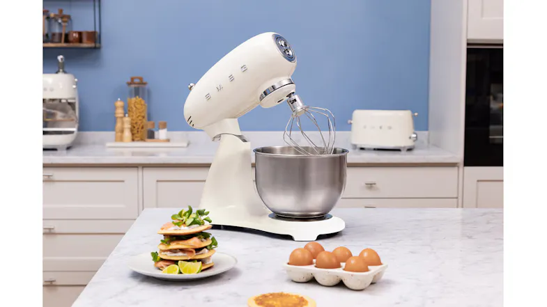 Smeg stand mixer with whisk attachment and stainless steel bowl on a marble countertop Smeg stand mixer with whisk attachment and stainless steel bowl on a marble countertop