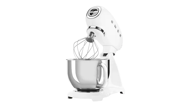 Angled side view of the Smeg stand mixer with tilt head raised and whisk attachment over the stainless steel bowl Angled side view of the Smeg stand mixer with tilt head raised and whisk attachment over the stainless steel bowl