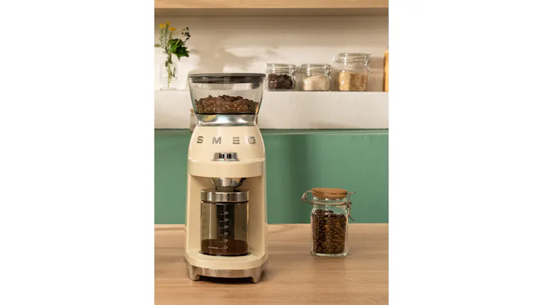 A side-by-side view of a Smeg coffee grinder and a jar of coffee beans in a kitchen counter setup A side-by-side view of a Smeg coffee grinder and a jar of coffee beans in a kitchen counter setup