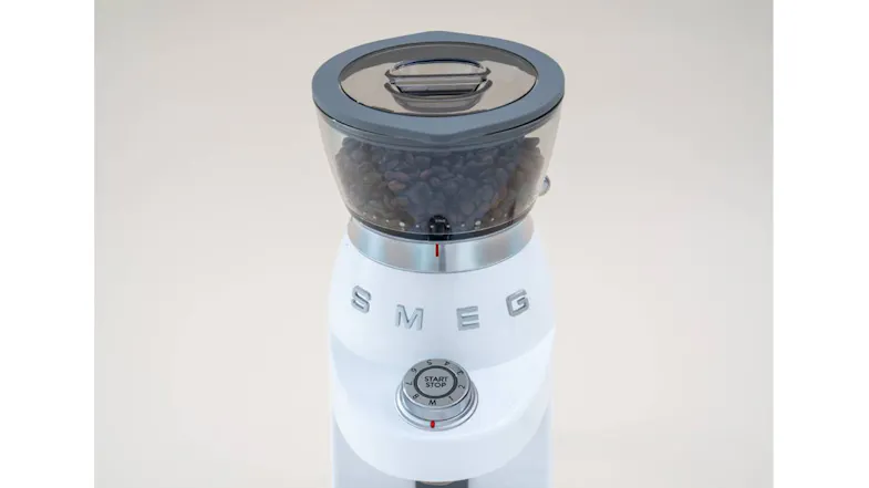 A top view of a coffee grinder filled with beans, showing the grey lid and start-stop dial under soft lighting A top view of a coffee grinder filled with beans, showing the grey lid and start-stop dial under soft lighting