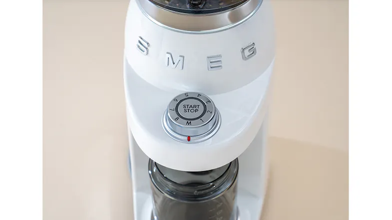 A close-up of a coffee grinder dial labelled “Start Stop” with a red indicator, a glossy white finish and silver trim A close-up of a coffee grinder dial labelled “Start Stop” with a red indicator, a glossy white finish and silver trim