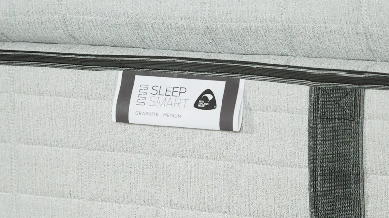 Detailed view of the tag on the mattress reading "Sleep Smart" and "Graphite - Medium” Detailed view of the tag on the mattress reading "Sleep Smart" and "Graphite - Medium”