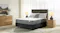 A fully dressed bed with a dark grey base sits in a brightly lit, modern bedroom between two light wood nightstands A fully dressed bed with a dark grey base sits in a brightly lit, modern bedroom between two light wood nightstands