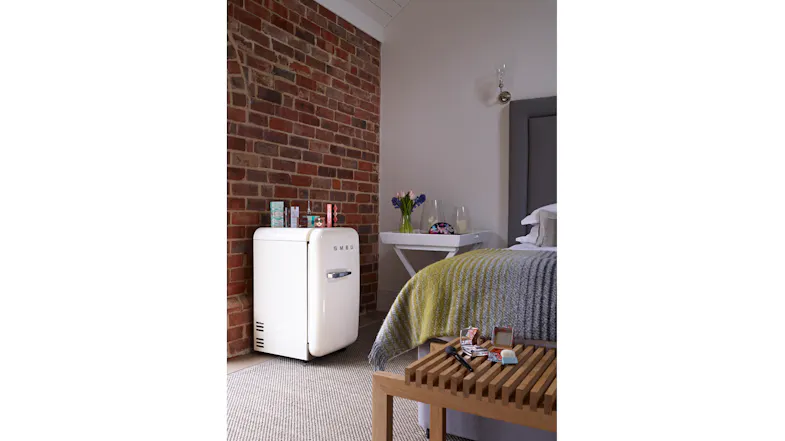 Stylish mini fridge next to the bed in a modern bedroom with a brick wall and decor pieces Stylish mini fridge next to the bed in a modern bedroom with a brick wall and decor pieces