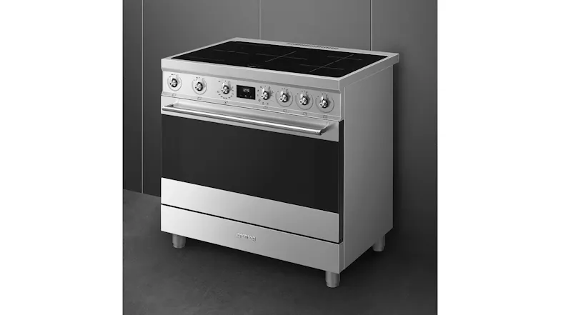 Angled view of a stainless steel induction range cooker with a black glass oven door and control knobs Angled view of a stainless steel induction range cooker with a black glass oven door and control knobs