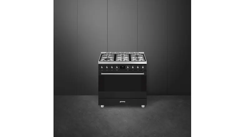 Full view of a black Smeg freestanding gas range against a dark wall, featuring a five-burner cooktop and oven Full view of a black Smeg freestanding gas range against a dark wall, featuring a five-burner cooktop and oven