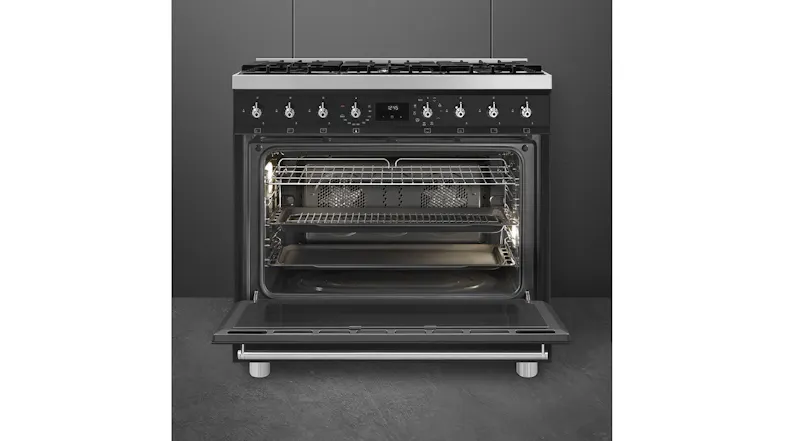 Open oven showing interior racks, tray, and rear fan, with control knobs and cooktop above Open oven showing interior racks, tray, and rear fan, with control knobs and cooktop above