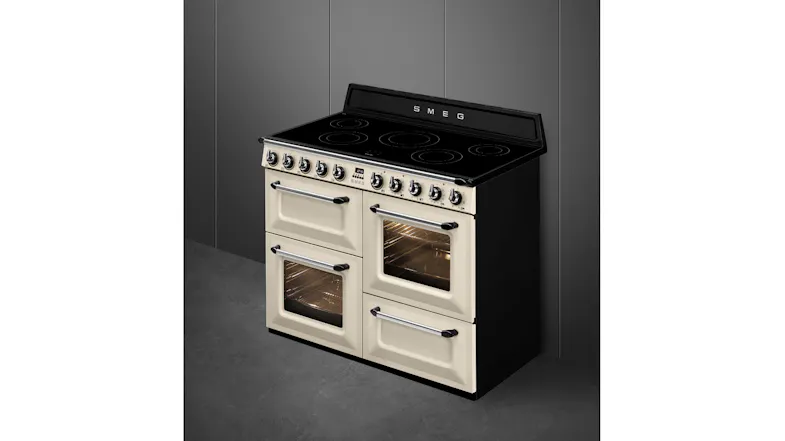 An angled view of a cream Smeg range cooker against a grey wall, featuring two oven windows glowing with warm interior light An angled view of a cream Smeg range cooker against a grey wall, featuring two oven windows glowing with warm interior light