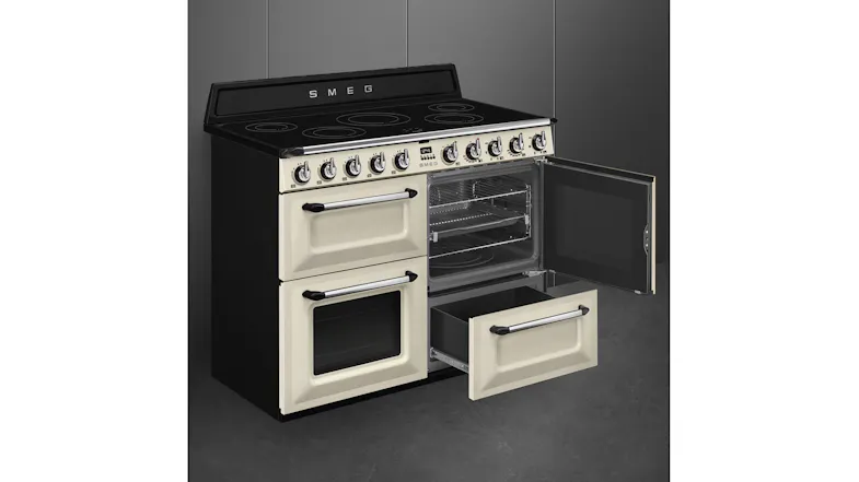A right-angled view of a cream Smeg range cooker with one oven door open and the storage drawer pulled out A right-angled view of a cream Smeg range cooker with one oven door open and the storage drawer pulled out