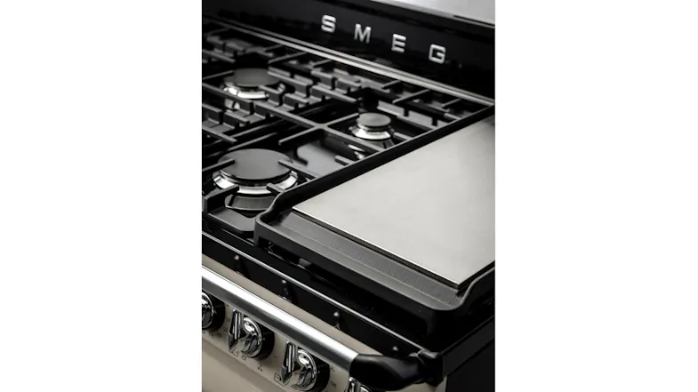 A close-up angled shot of the gas cooktop on a cream Smeg Victoria cooker, featuring a flat silver teppanyaki griddle plate A close-up angled shot of the gas cooktop on a cream Smeg Victoria cooker, featuring a flat silver teppanyaki griddle plate