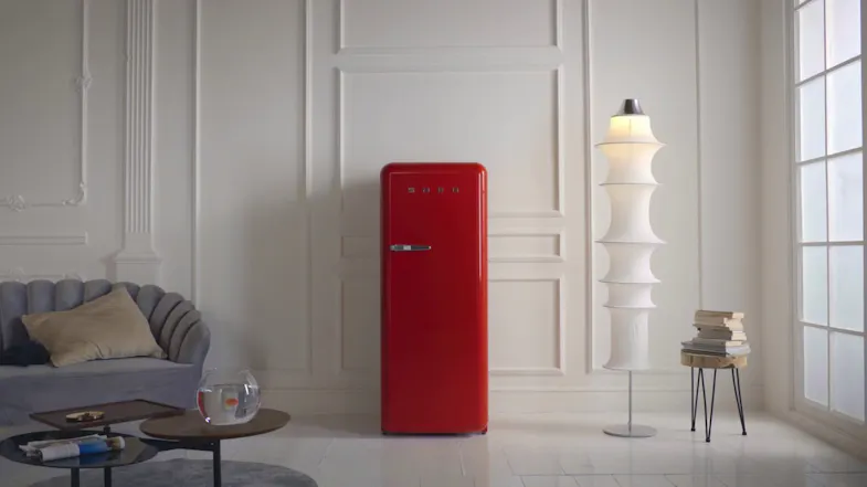 Red SMEG retro refrigerator in a bright living space with a sofa, floor lamp, side table, and window Red SMEG retro refrigerator in a bright living space with a sofa, floor lamp, side table, and window