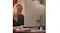 Rear view of the HP 27-inch all-in-one desktop in shell white on a desk, with a person seated nearby Rear view of the HP 27-inch all-in-one desktop in shell white on a desk, with a person seated nearby