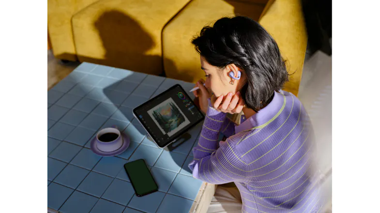 High-angle view of a woman wearing an earbud while looking at a tablet High-angle view of a woman wearing an earbud while looking at a tablet