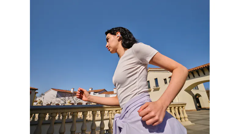 Side view of a person walking near a concrete structure with wireless earbuds Side view of a person walking near a concrete structure with wireless earbuds