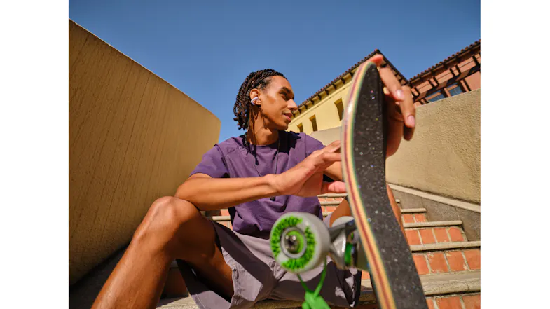 Low-angle view of a person holding a skateboard outdoors with earbuds Low-angle view of a person holding a skateboard outdoors with earbuds