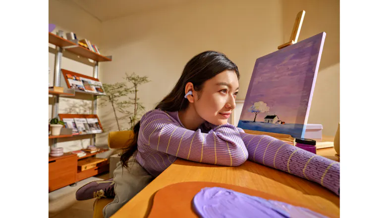 Side view of a woman looking at a desktop monitor with purple earbuds Side view of a woman looking at a desktop monitor with purple earbuds