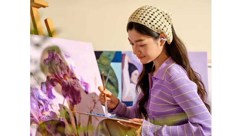 Close-up view of a woman painting a floral canvas artwork with matching earbuds Close-up view of a woman painting a floral canvas artwork with matching earbuds