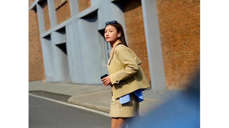 Full-body view of a person in a blazer walking outdoors with Shokz earbuds Full-body view of a person in a blazer walking outdoors with Shokz earbuds