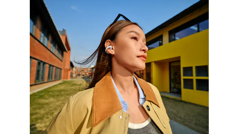 Front view of a woman with an earbud looking upward near colourful architecture Front view of a woman with an earbud looking upward near colourful architecture