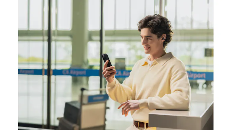 Lifestyle view of a man looking at his phone indoors while wearing earbuds Lifestyle view of a man looking at his phone indoors while wearing earbuds