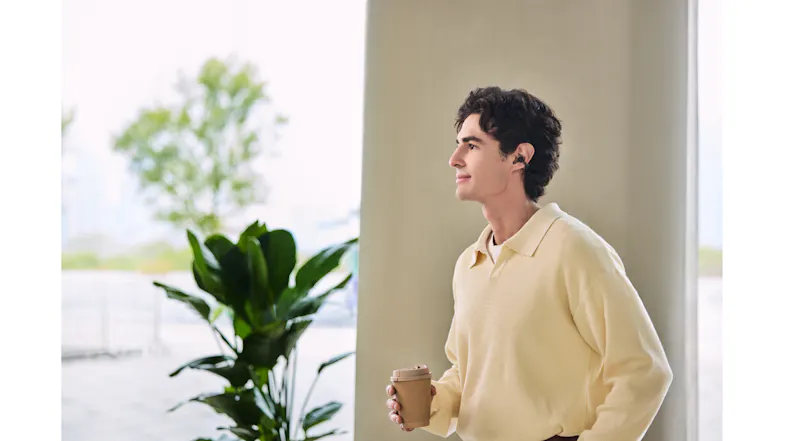 Profile view of a man standing indoors wearing black earbuds Profile view of a man standing indoors wearing black earbuds