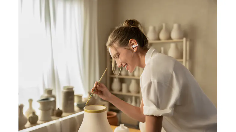 Indoor view of a woman painting pottery while wearing earbuds Indoor view of a woman painting pottery while wearing earbuds