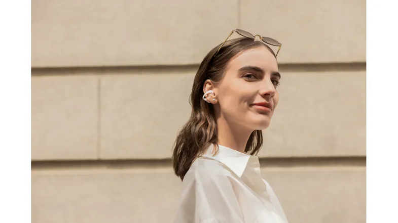 Profile view of a person standing near a building wall with an earbud Profile view of a person standing near a building wall with an earbud