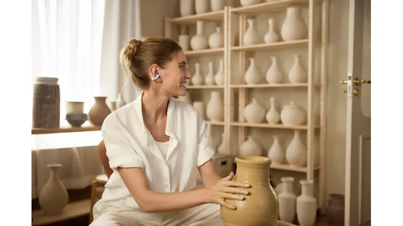 A woman arranging ceramic pottery on shelves with an earbud A woman arranging ceramic pottery on shelves with an earbud