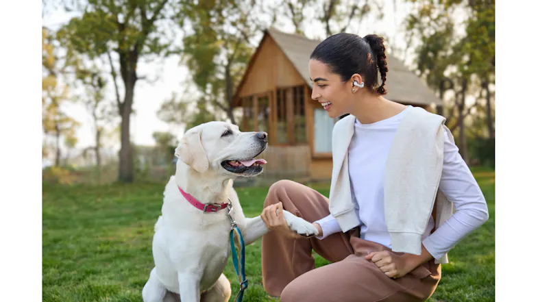 A woman wearing Shokz earbuds while playing with her dog outdoors A woman wearing Shokz earbuds while playing with her dog outdoors