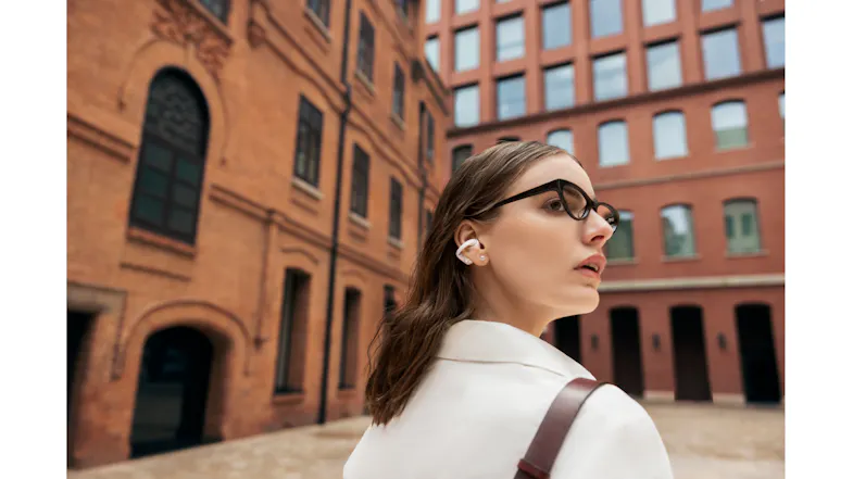 Low-angle view of a person with white earbuds looking up near brick architecture Low-angle view of a person with white earbuds looking up near brick architecture