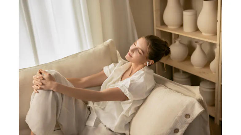 Indoor lifestyle view of a woman relaxing on a cosy sofa while wearing earbuds Indoor lifestyle view of a woman relaxing on a cosy sofa while wearing earbuds