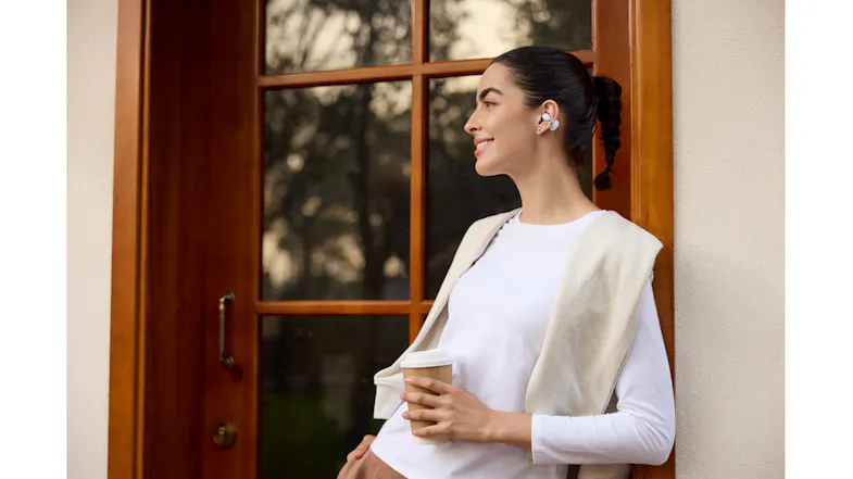 A woman with an earbud is holding a beverage cup by a doorway A woman with an earbud is holding a beverage cup by a doorway