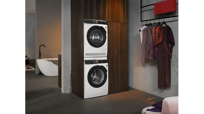 Stacked washer and dryer built into a modern closet space beside a bathroom, and hanging clothes Stacked washer and dryer built into a modern closet space beside a bathroom, and hanging clothes