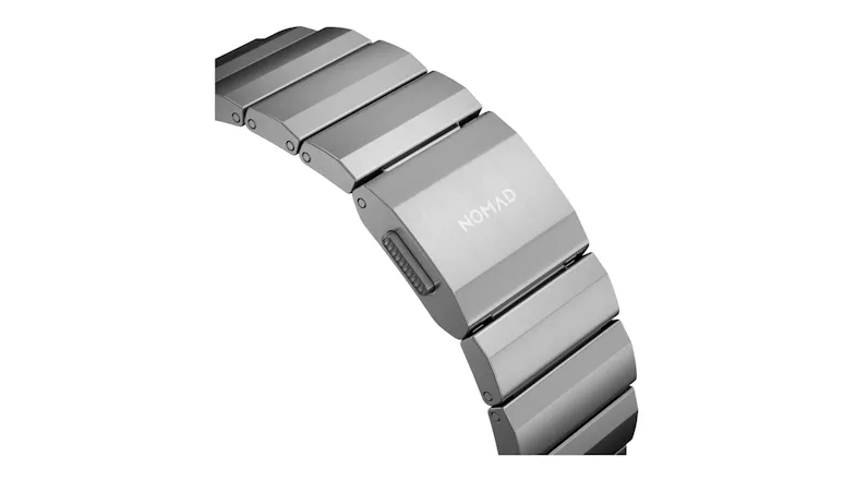 Close-up of a silver metal link band clasp with a brushed titanium finish and Nomad branding Close-up of a silver metal link band clasp with a brushed titanium finish and Nomad branding