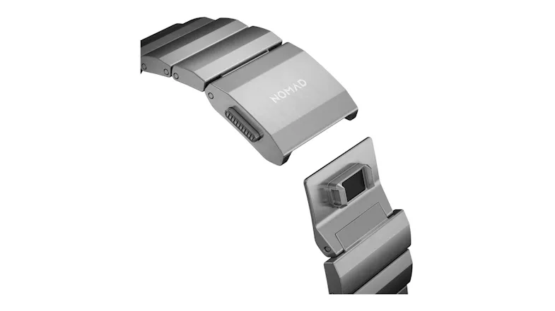Close-up of a silver titanium watch band clasp with a magnetic lock mechanism and Nomad branding Close-up of a silver titanium watch band clasp with a magnetic lock mechanism and Nomad branding