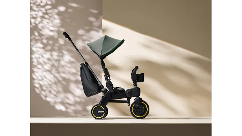 Angled view of a green toddler tricycle with a canopy and push handle shown in a stylish lifestyle setting Angled view of a green toddler tricycle with a canopy and push handle shown in a stylish lifestyle setting