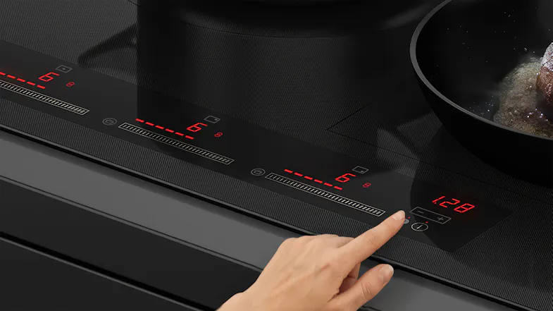 Close-up of the Fisher & Paykel cooktop touch controls. A hand adjusts the settings Close-up of the Fisher & Paykel cooktop touch controls. A hand adjusts the settings