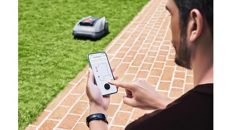 A man is controlling the lawn mower via its compatible app A man is controlling the lawn mower via its compatible app